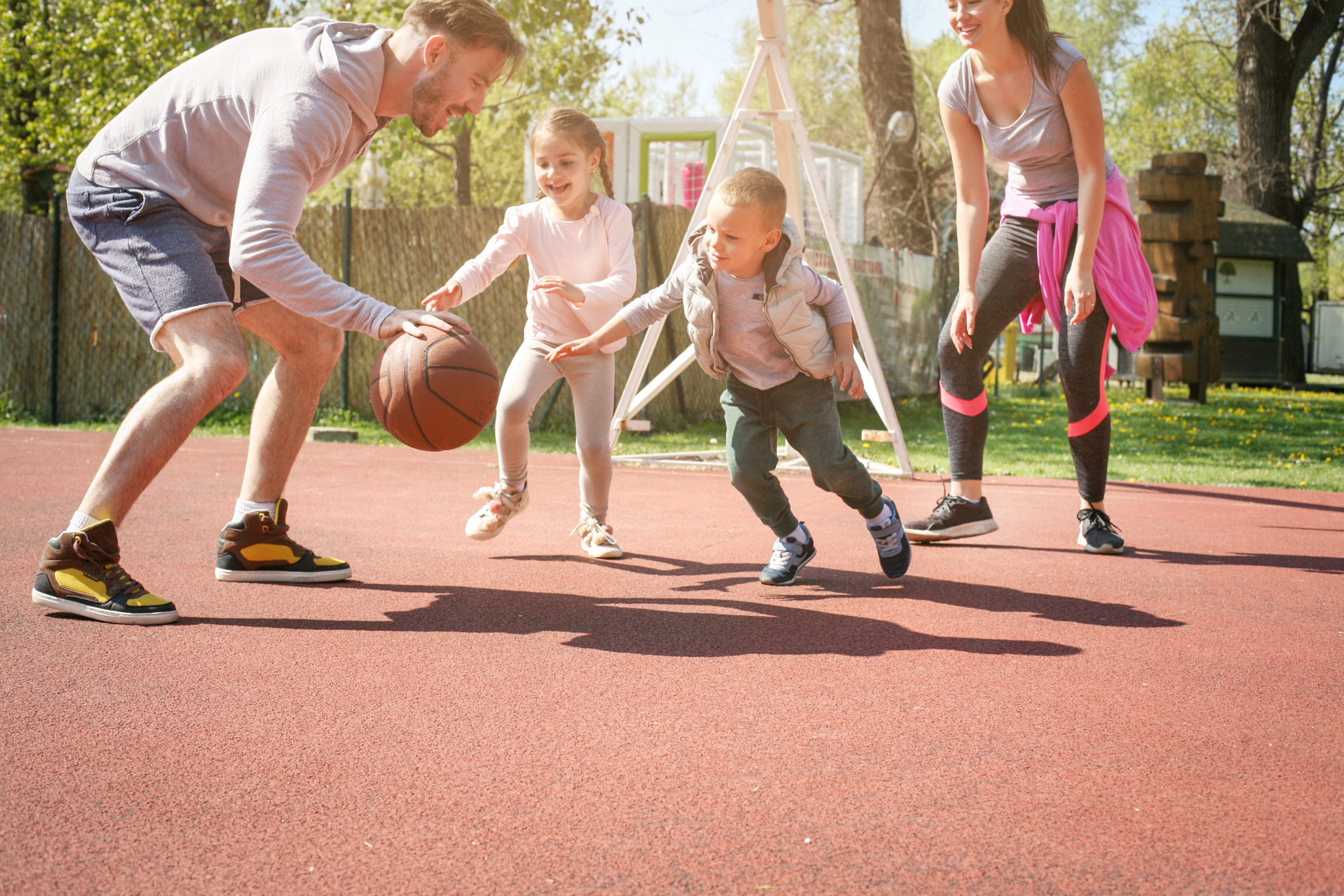 A father and mother play basketball in the spring with their two children. 